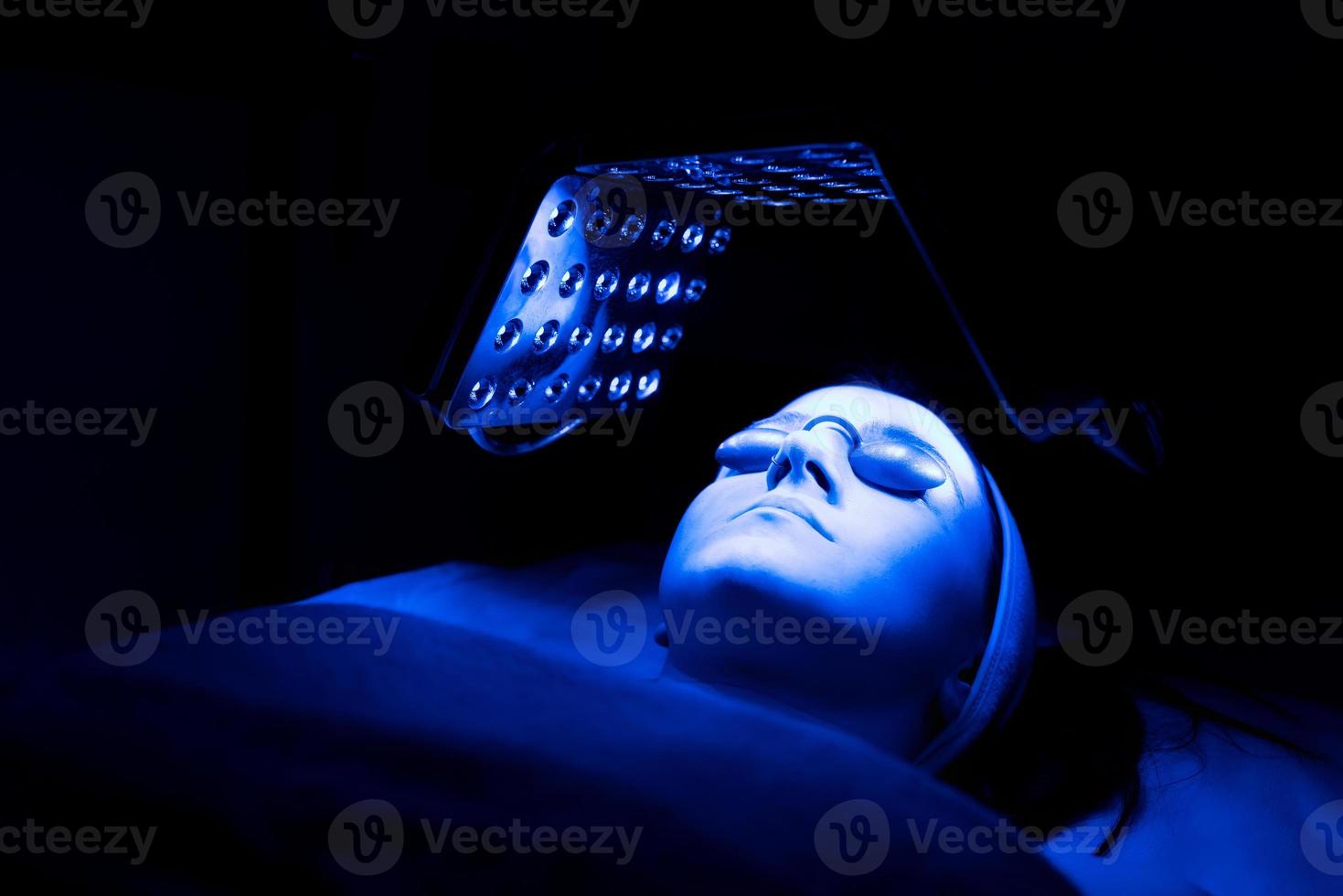 Young woman having blue LED light facial therapy treatment in beauty salon. photo