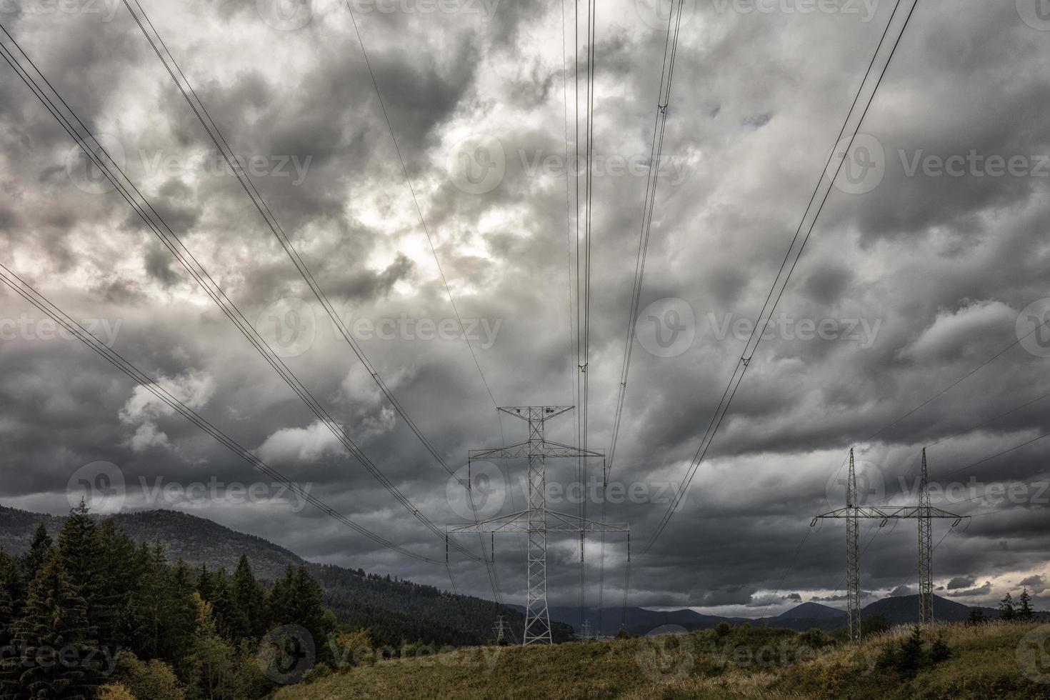 High voltage towers with electricity transmission power lines in country under dark clouds photo