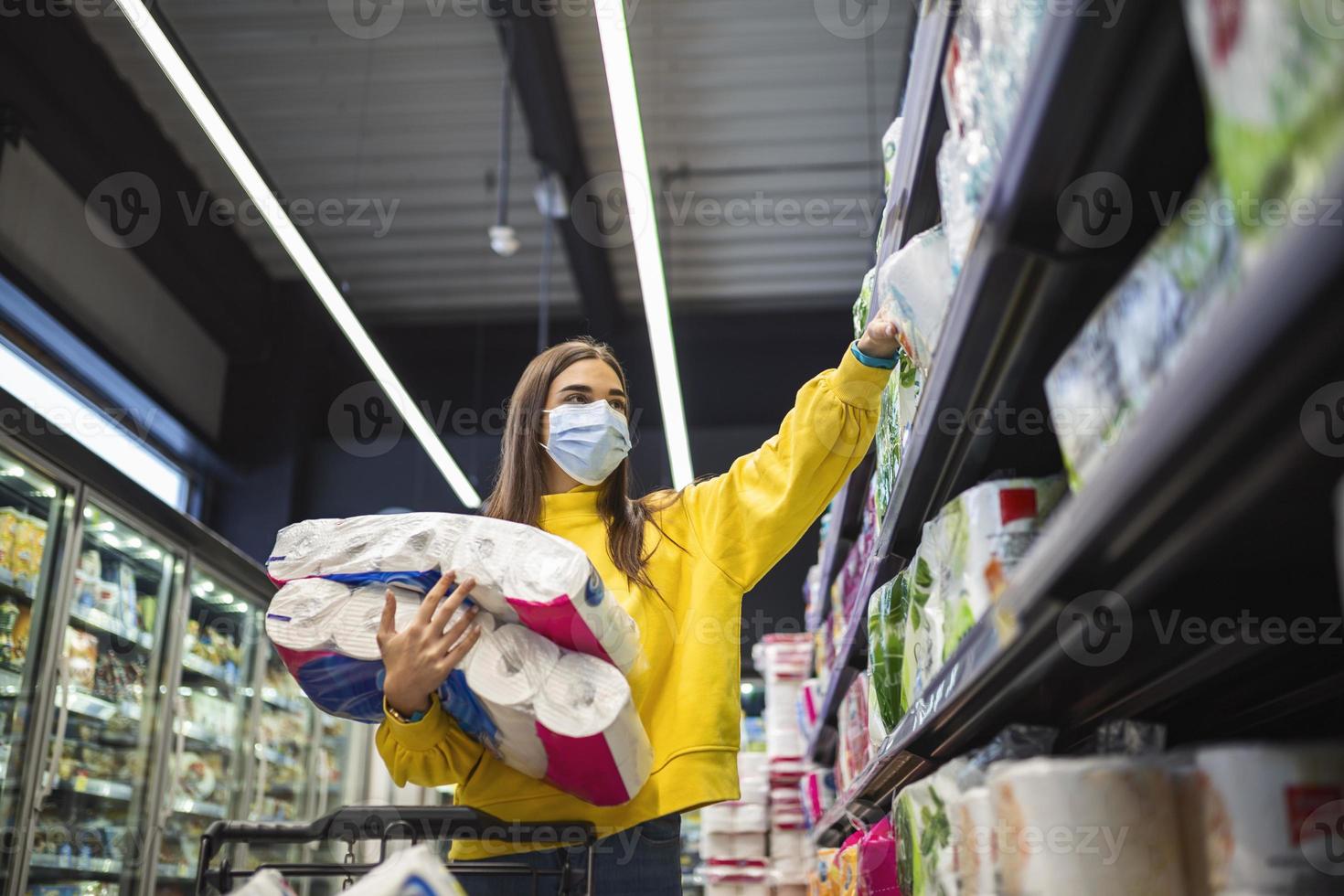 Escasez de papel higiénico. mujer con máscara higiénica que compra suministros de papel higiénico debido a la compra de pánico y al acaparamiento de productos durante el brote epidémico de virus. deficiencia de productos de higiene foto de archivo