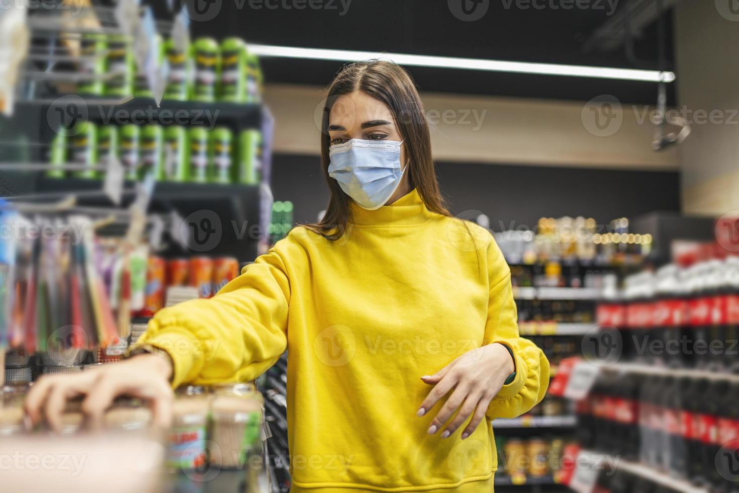 mujer con máscara protectora y comprando comida en la tienda de comestibles durante la epidemia de virus. mujer joven con una máscara protectora y guantes comprando en un momento de pandemia de virus, comprando suministros de alimentos foto