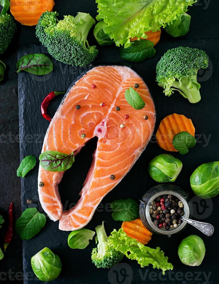 Raw salmon steak and ingredients for cooking on a dark background in a rustic style. Top view photo
