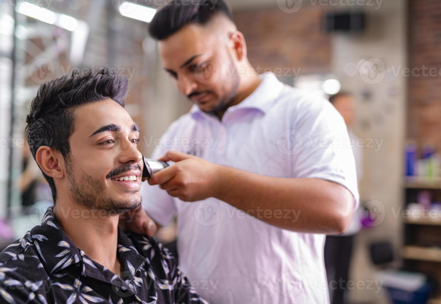 Handsome Arab man is getting shaved by hairdresser at the barbershop photo