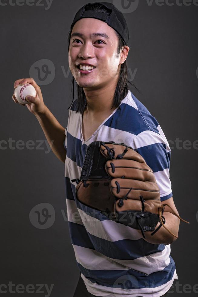 modelo masculino asiático con guante de béisbol aislado sobre fondo oscuro. concepto de jugador de béisbol foto