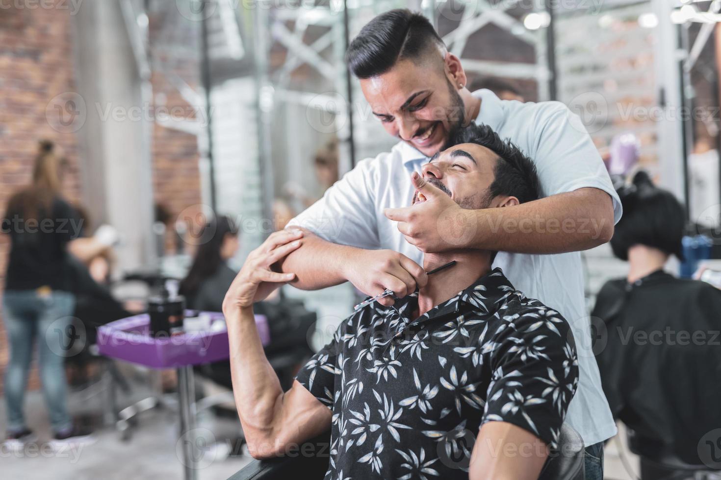 Handsome Arab man is getting shaved by hairdresser at the barbershop photo