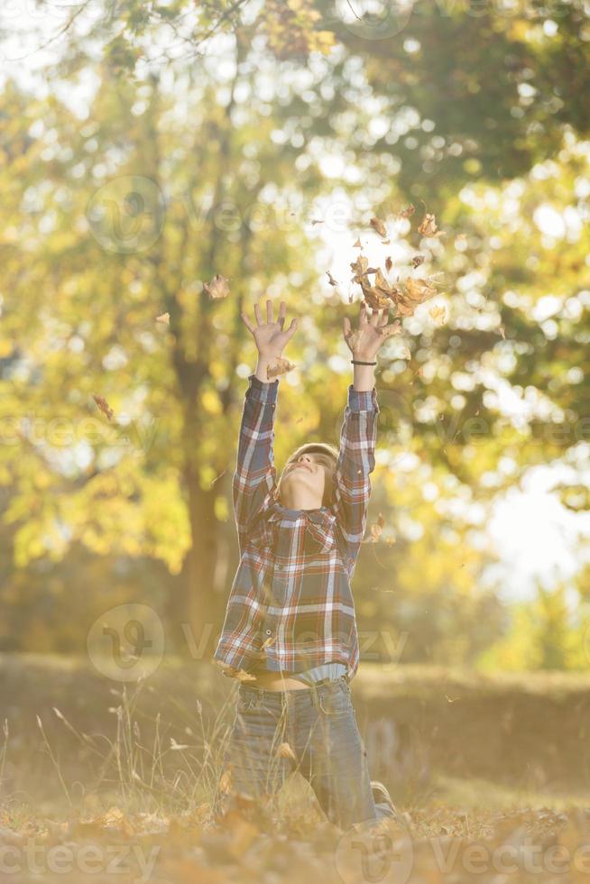 adorable niñito jugando con hojas amarillas en el soleado parque de otoño foto