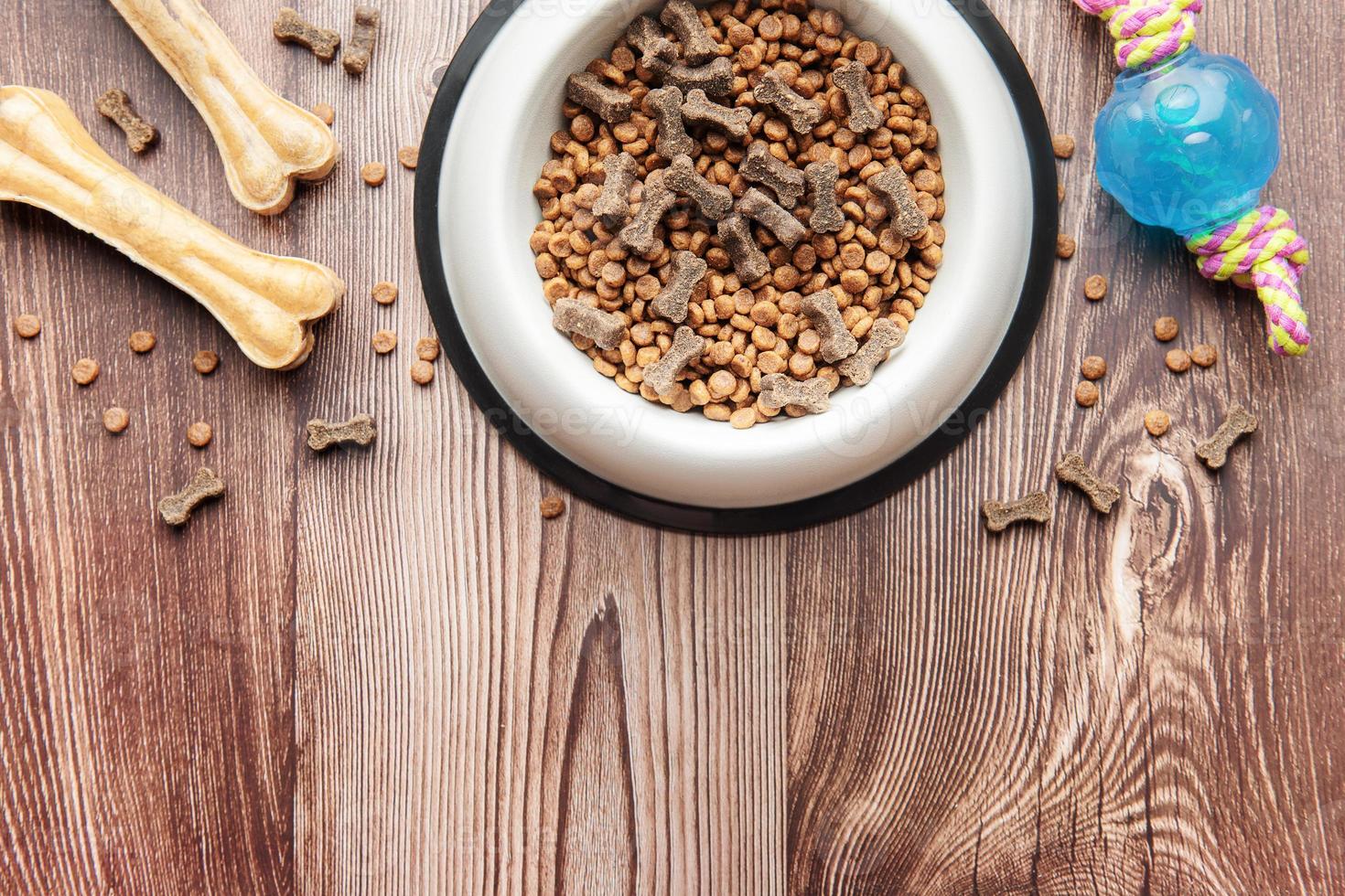 A bowl with dog food, dog treats and toys on a wooden floor. photo