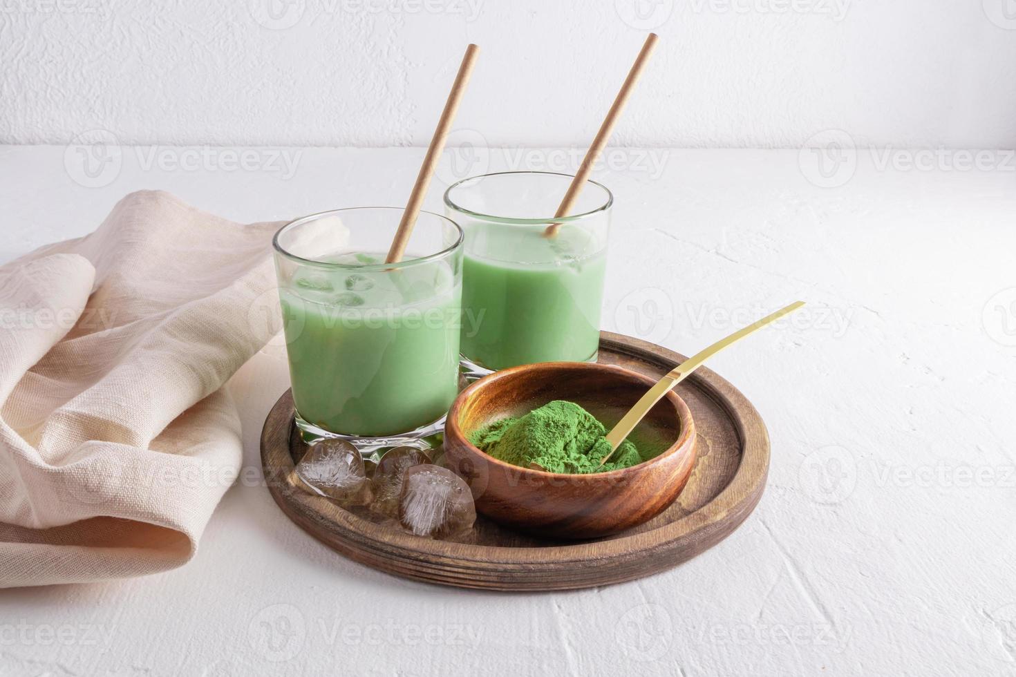 delicious healthy matcha latte tea in two glasses with straw and ice pieces on a round wooden tray. an alternative to coffee. invigorating drink. photo