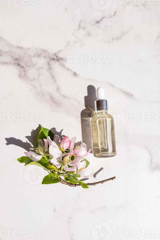 vista vertical superior de una botella con una pipeta con un suero hidratante para rejuvenecer la piel de la cara. cosmética natural. flores de manzana rosa. foto