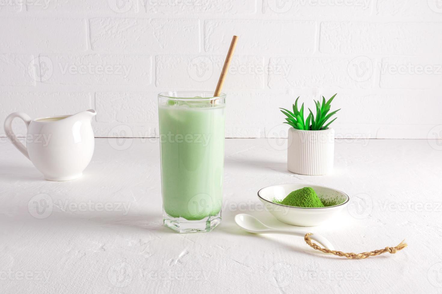 a glass of matcha latte tea and straw against a white brick wall. a bowl of green tea powder. healthy tea. the concept of healing, cleansing. photo