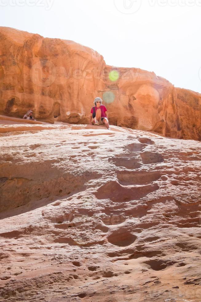 joven mujer caucásica baja de la formación rocosa enfrenta sus miedos en la naturaleza en el desierto de wadi rum en la gira del desierto de vacaciones foto