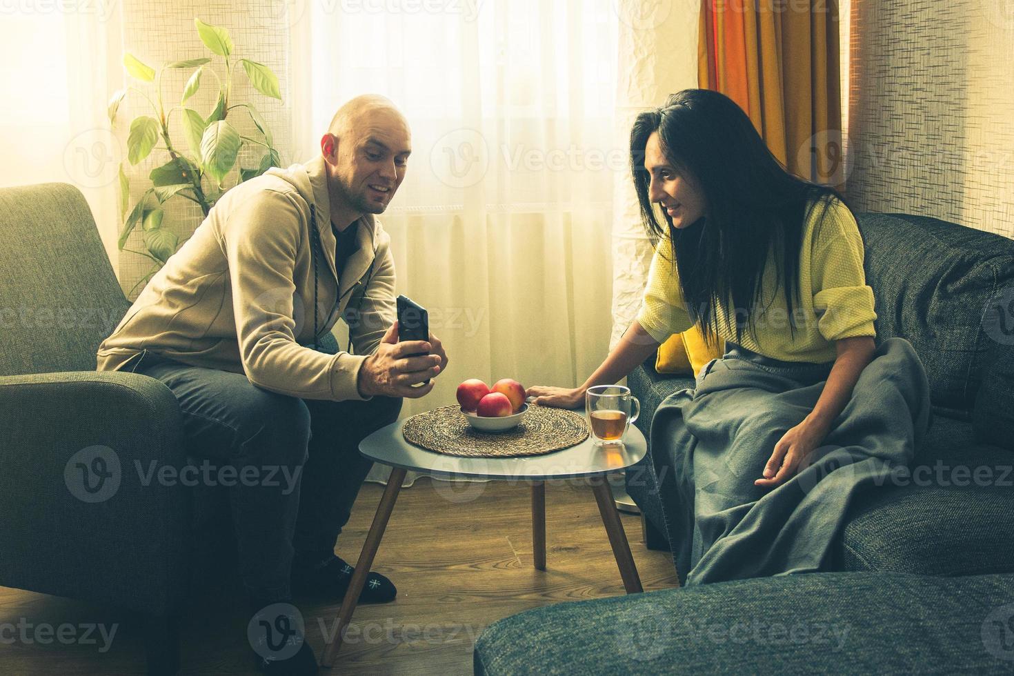 Caucasian man show on phone screen offer deal discount while Sitting on Couch Cozy Apartment do e-Shopping on Internet, Watching Funny Videos, Use Social Media, Streaming Service photo