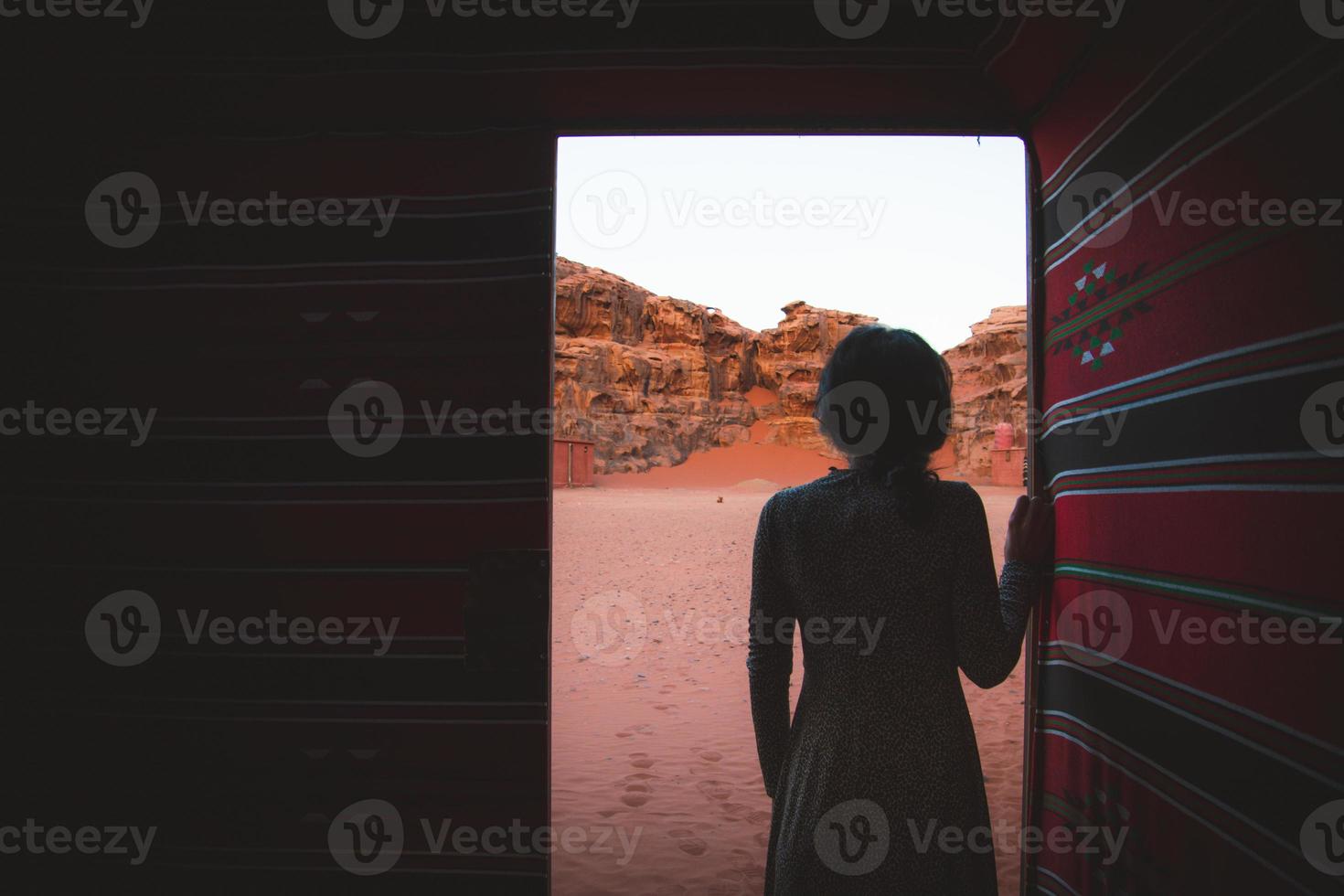 Woman person stand in desert bedouin camp inside traditional tent with open door enjoy wadi rum desert cliffs and textures early morning photo