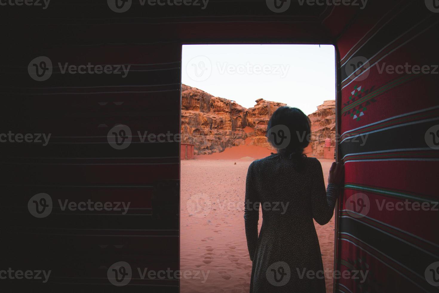 mujer persona de pie en el campamento beduino del desierto dentro de una tienda tradicional con puerta abierta disfrutar de los acantilados y texturas del desierto de wadi rum temprano en la mañana foto