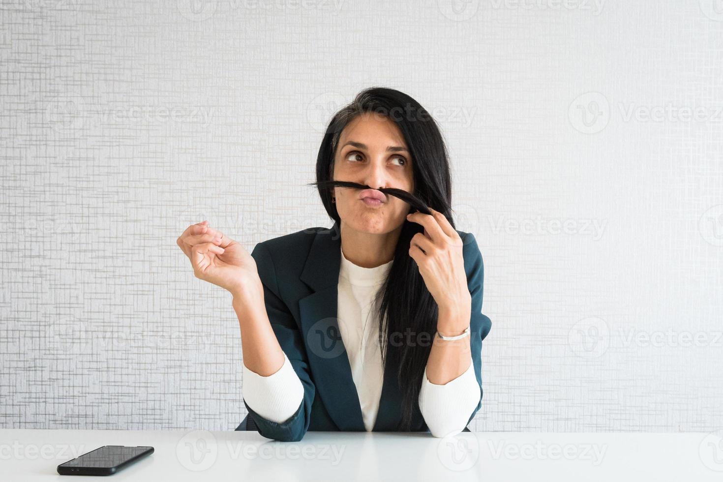 joven mujer de negocios morena caucásica directora en la oficina jugar pelo hacer cara de pescado. mujer de negocios aburrida pasando tiempo en la oficina. trabajador corporativo perezoso postergando el trabajo foto