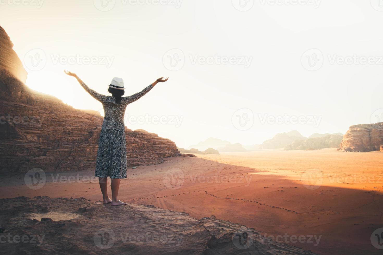 Happy celebrating winning success woman at sunset or sunrise standing elated with arms raised up in celebration of having reached mountain top summit goal during hiking travel trek photo