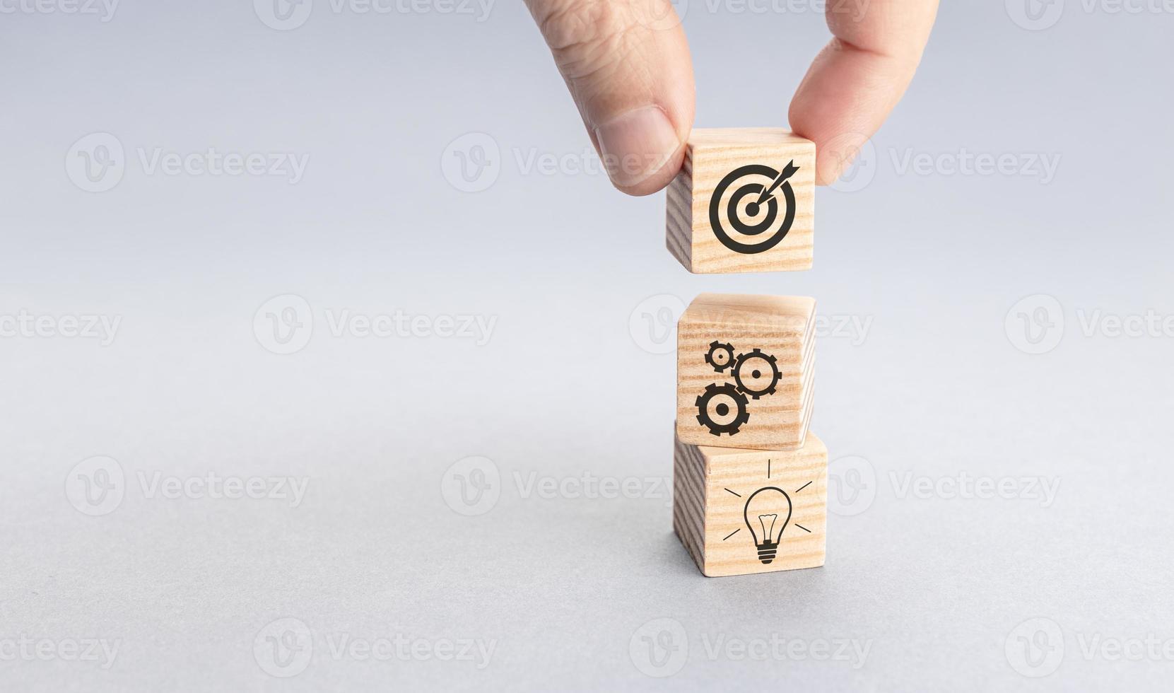 Business strategy and action plan concept. Hand putting wood block with target icon on top of others with gear and light bulb icons. Gray background. Copy space photo