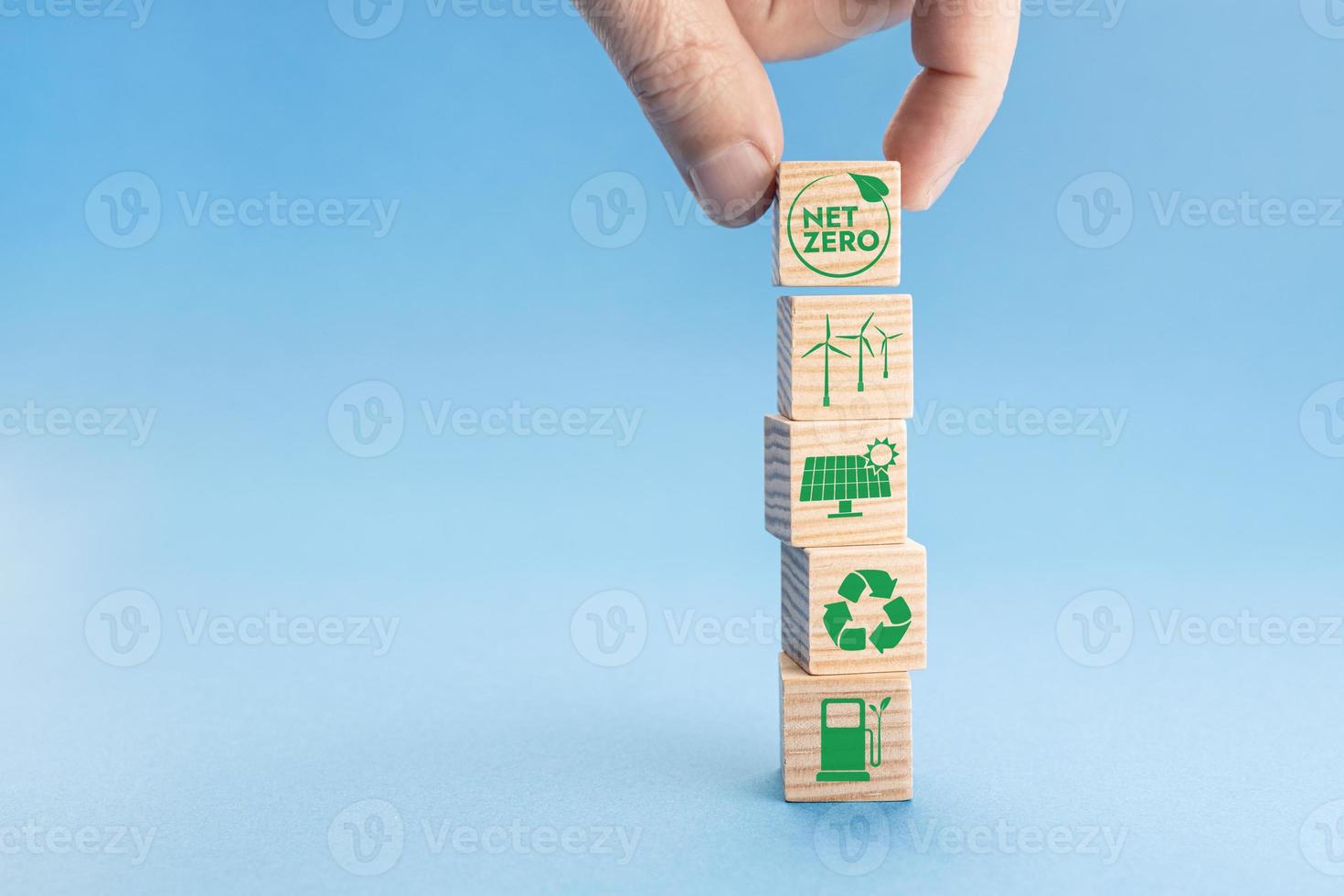 Net Zero and Carbon Neutral Concept. Hand putting wood block with Net Zero icon on top of others with green energy icons. Blue background. Copy space photo