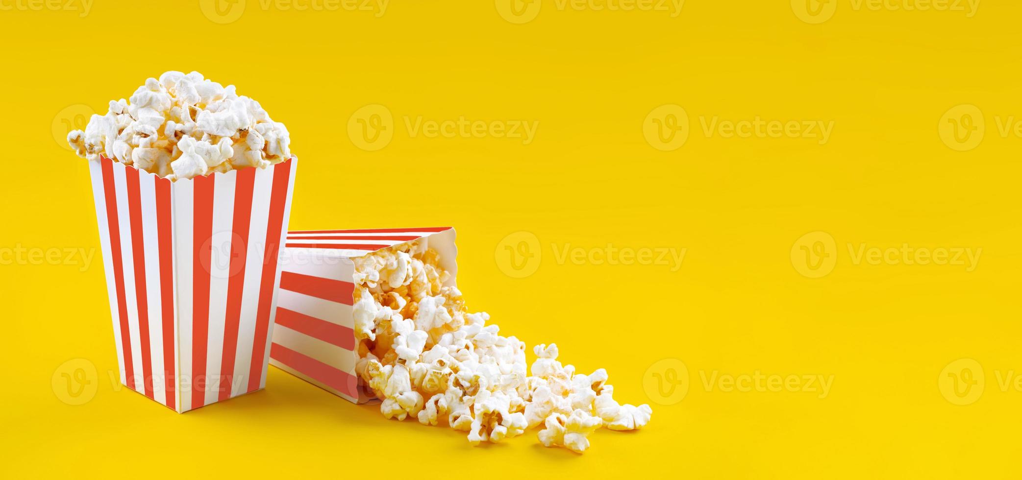 Two red white striped carton buckets with tasty cheese popcorn, isolated on yellow background photo