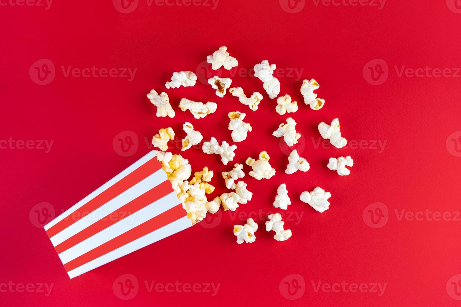 Tasty cheese popcorn falling out of a red striped carton bucket, isolated on red background photo