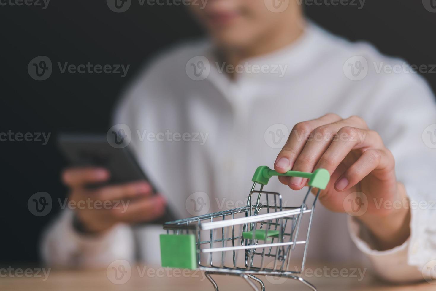 mano de hombre agarrando un carrito de compras, sociedad de consumo, concepto de adicción a las compras, servicio de compras en la web en línea y ofrece entrega a domicilio, conectando comerciantes y clientes de todo el mundo, pago en línea foto