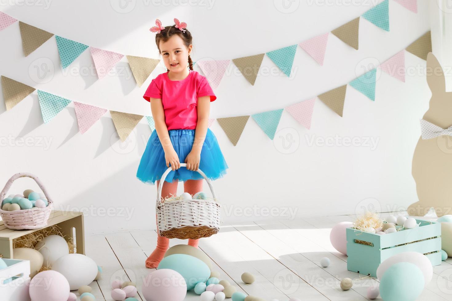 Getting ready to Easter. Lovely little girl holding an Easter egg and smiling with decoration in the background photo