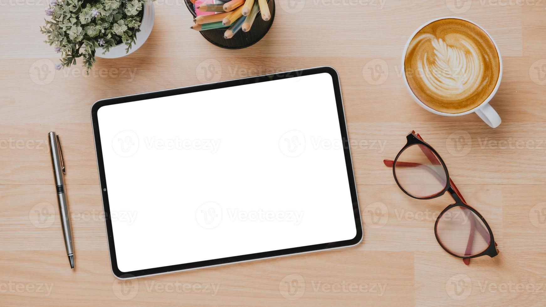 escritorio de madera de oficina con tableta de pantalla en blanco, bolígrafo, anteojos y taza de café, vista superior flay lay. foto