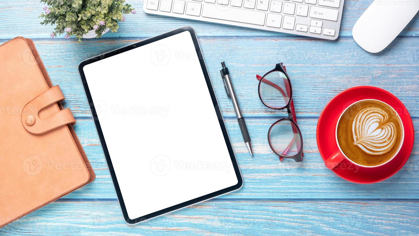 Tablet with blank screen, laptop computer, notebook, eyeglass, pen and cup of coffee on wooden desk, Top view flat lay. photo