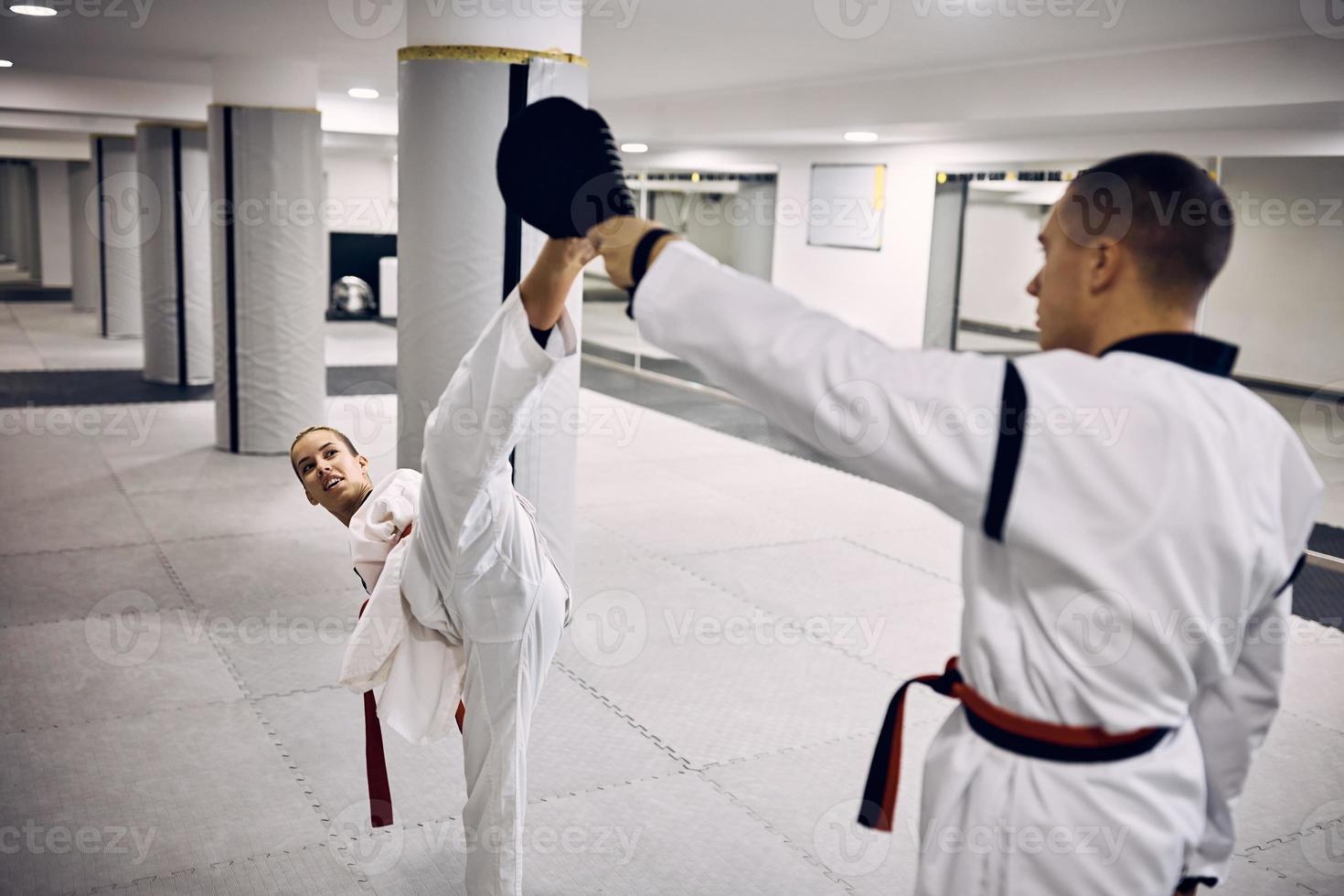 joven luchadora de taekwondo con discapacidad practicando patada alta con su entrenador en el club de salud. foto