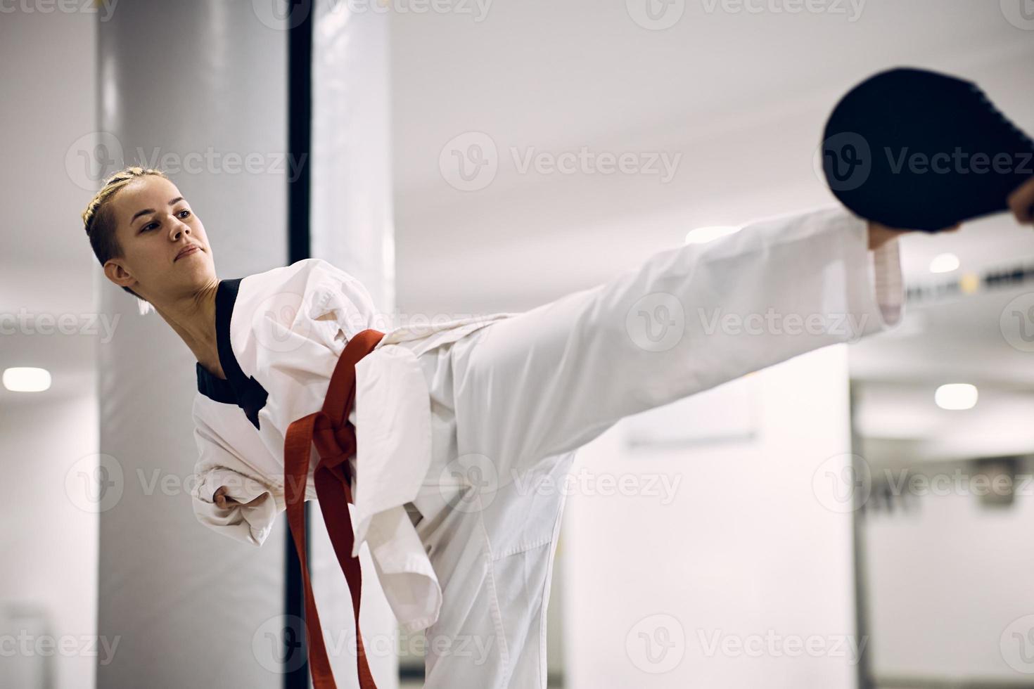 Female taekwondo fighter without the upper limbs exercising leg kick with a coach in health club. photo
