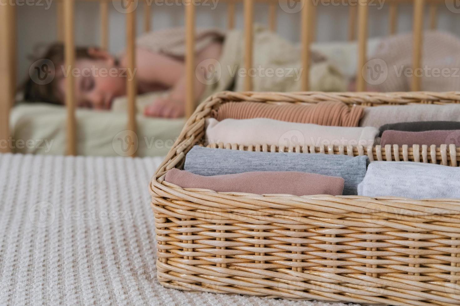 Baby clothes in a wicker container against the background of a sleeping baby. Vertical clothing storage photo