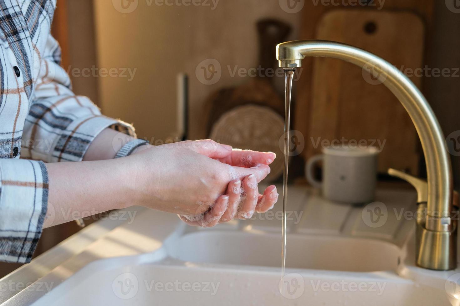 A woman washes her hands in the kitchen before dinner. Personal hygiene. Hand washing photo
