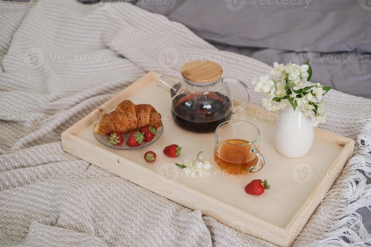 desayuno en la cama. bandeja con té, croissant y fresas en la cama del dormitorio foto