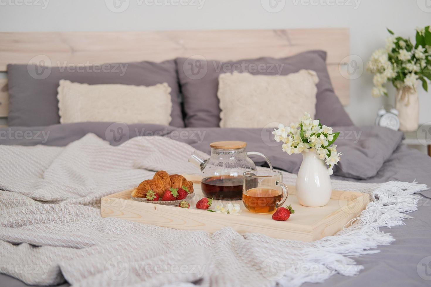 Breakfast in bed. Tray with tea, croissant and strawberries on the bed in the bedroom photo