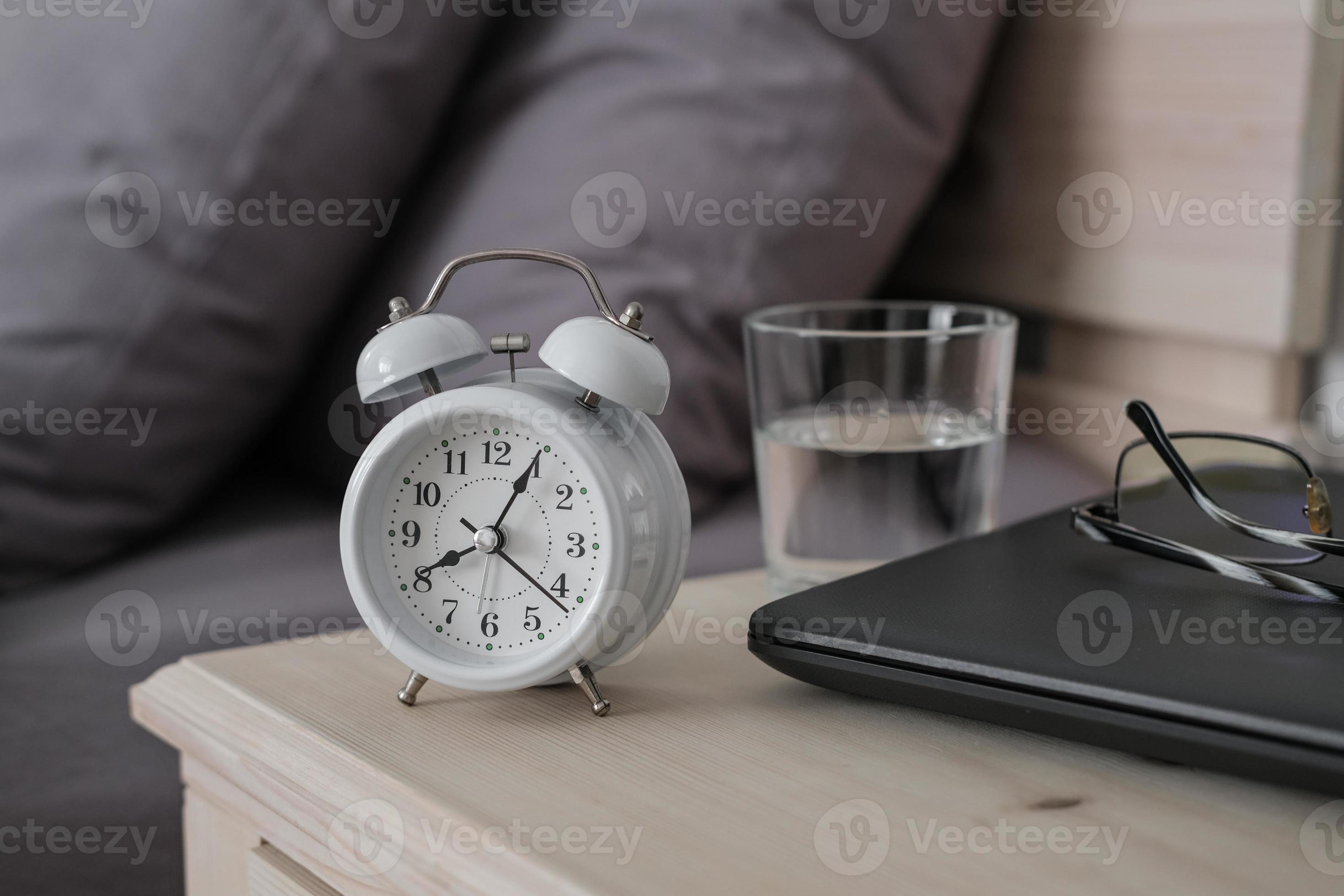 Alarm clock, laptop and glasses on the nightstand. Remote work in the