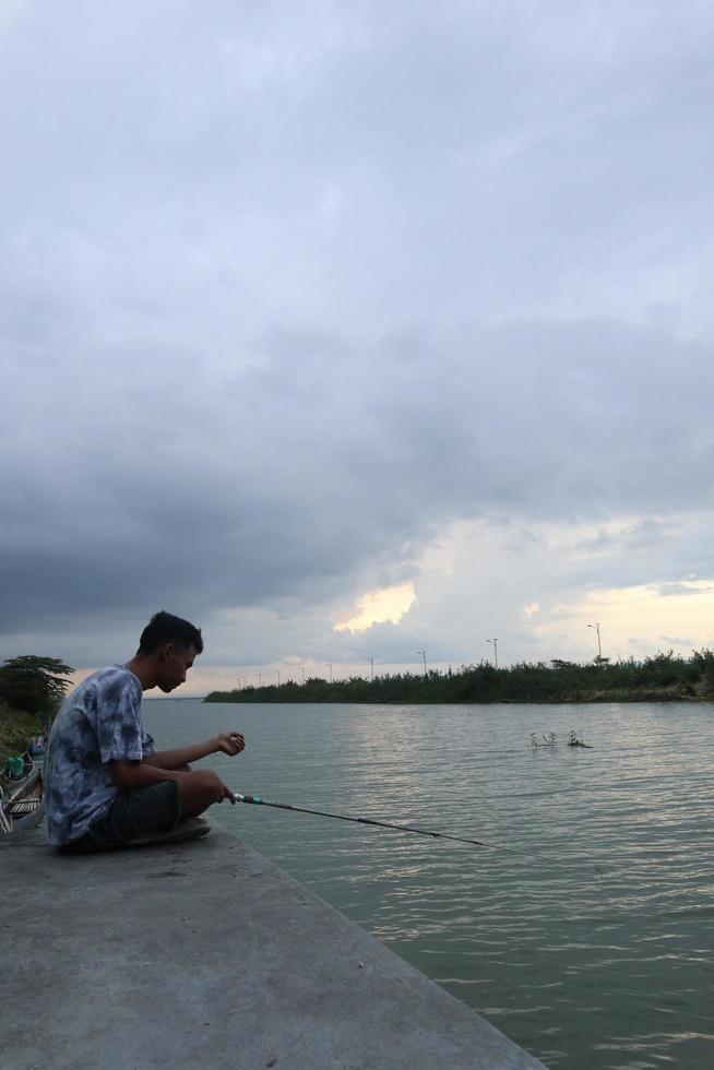 gorontalo-indonesia, diciembre de 2022 - un adolescente está pescando en la orilla del río por la tarde foto
