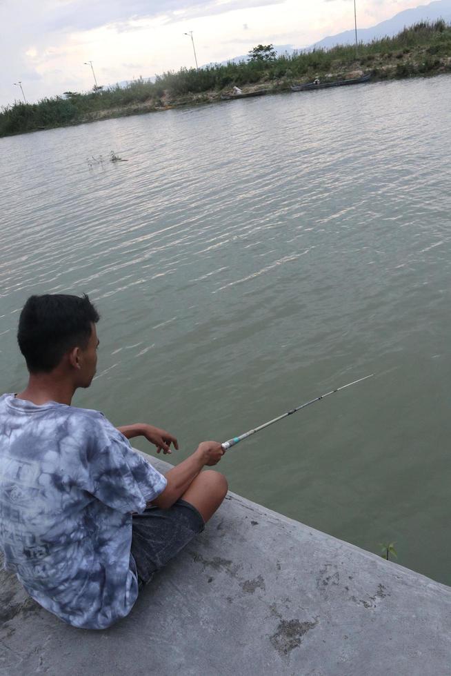 Gorontalo-Indonesia, December 2022 - A teenage boy is fishing on the riverbank in the afternoon photo