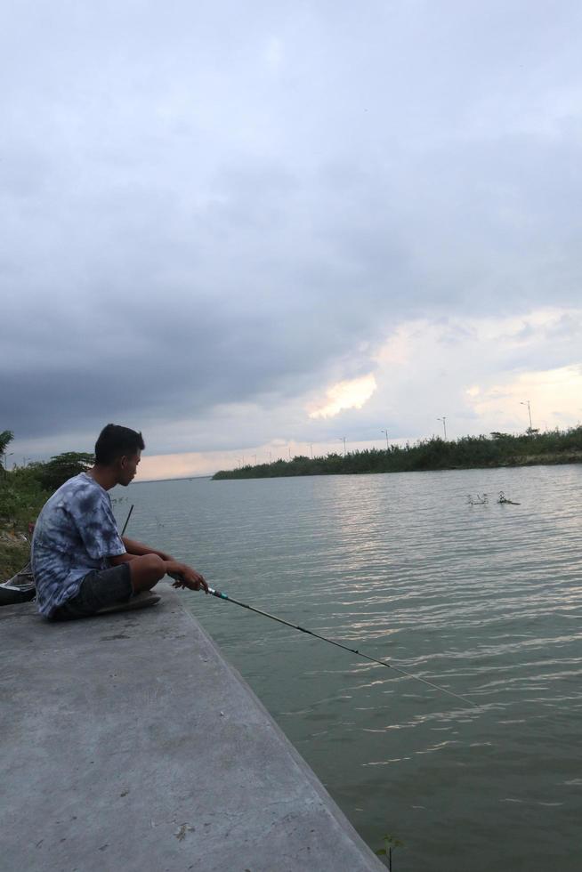 Gorontalo-Indonesia, December 2022 - A teenage boy is fishing on the riverbank in the afternoon photo