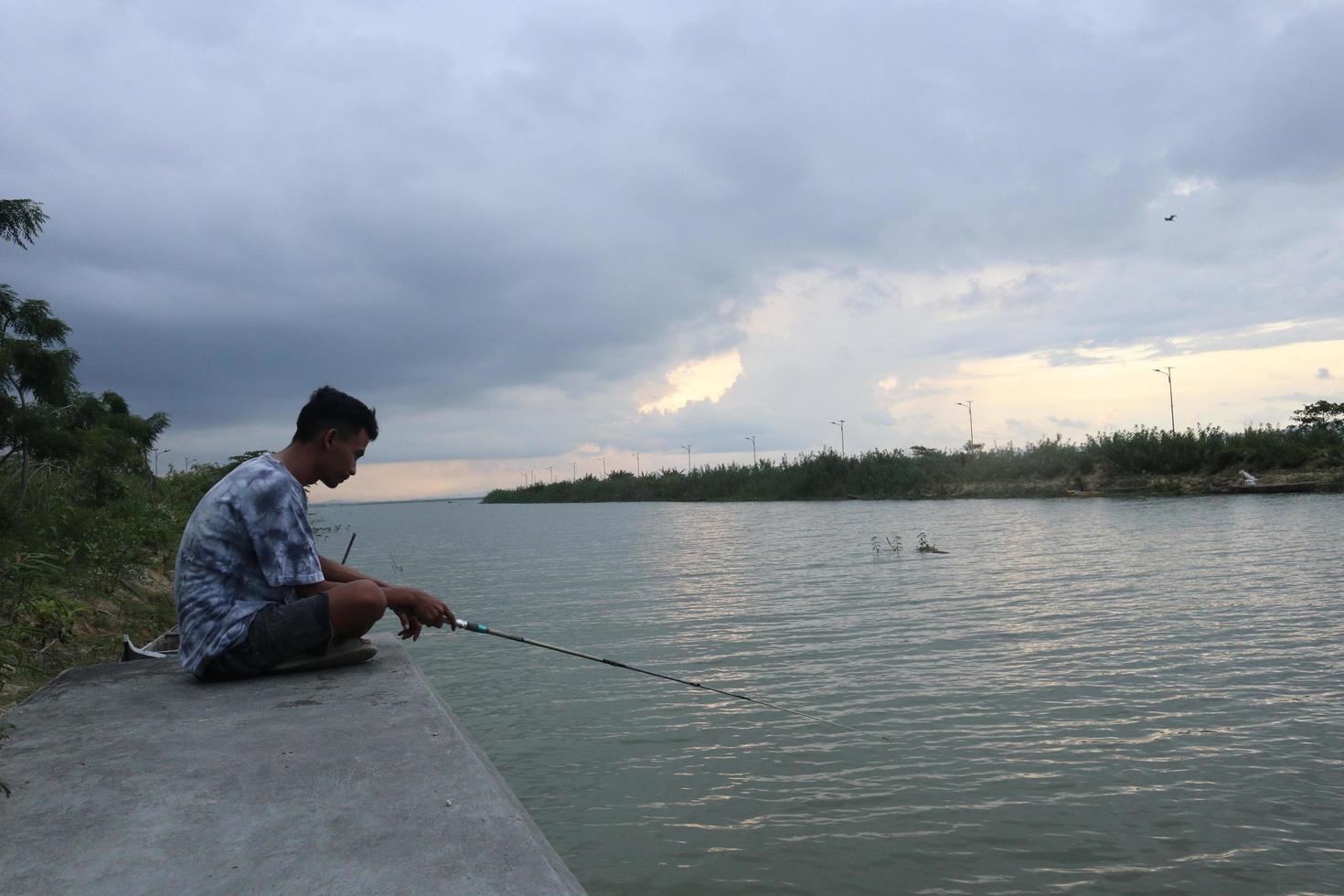 gorontalo-indonesia, diciembre de 2022 - un adolescente está pescando en la orilla del río por la tarde foto