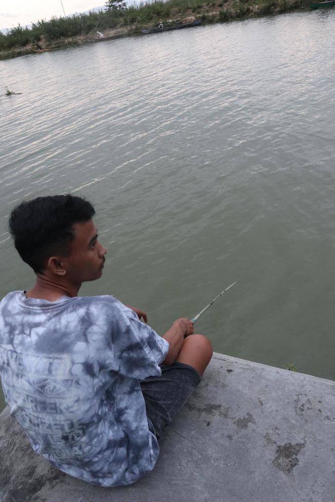 Gorontalo-Indonesia, December 2022 - A teenage boy is fishing on the riverbank in the afternoon photo