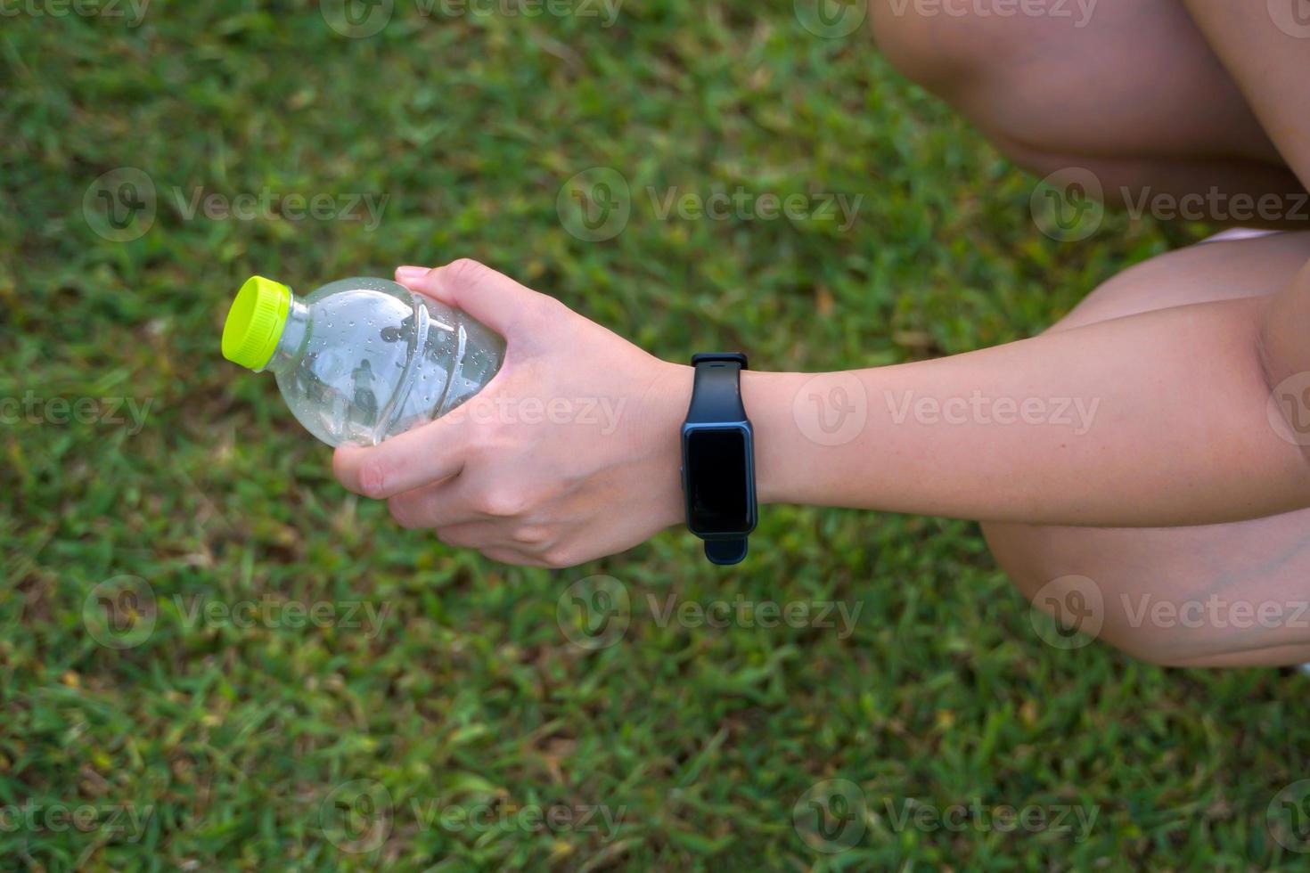 Asian woman wearing smartwatch, holding water bottle, she sits and drinks water during break, in concept, leisure activity, outside, exercise, outdoor activities photo