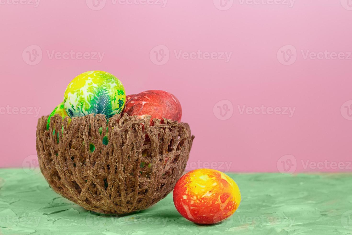 Colored eggs in nest on green and pink background. Easter. Copy space photo