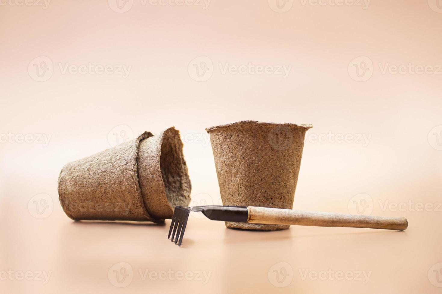 Eco-friendly organic peat pots with rake on brown background. Concept of gardening, planting. Monochrome. Copy space photo