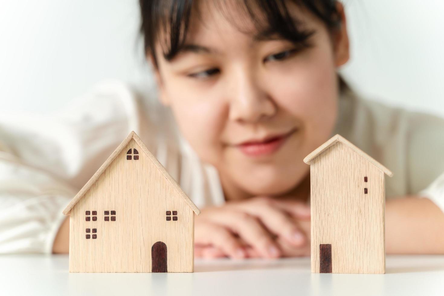 la mujer está decidiendo elegir una casa con un modelo de casa pequeña de madera, planeando comprar una propiedad. elegir lo que es mejor. conceptos de préstamos hipotecarios. foto