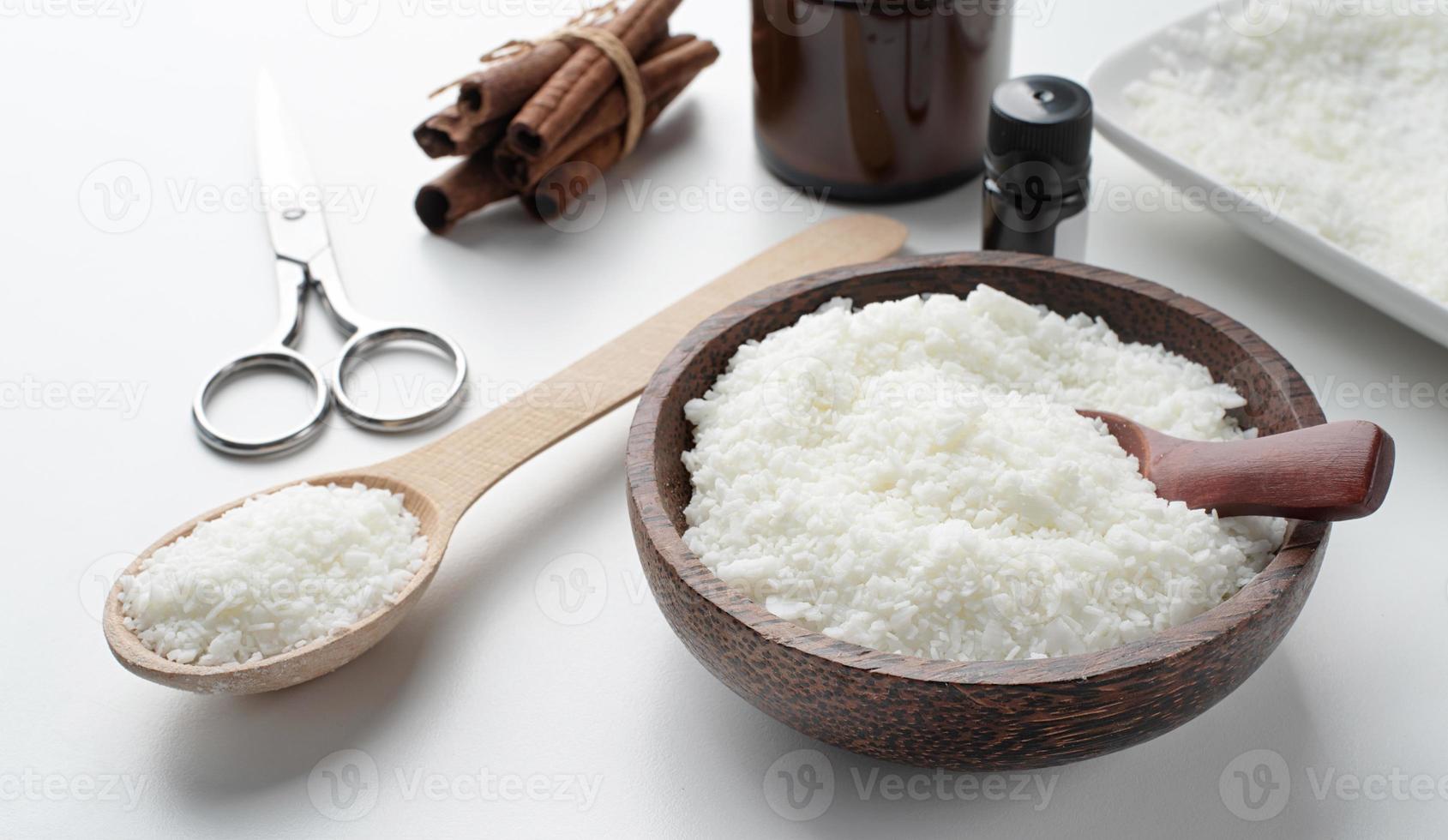 ingredients for candle making , soy wax flakes, candles, cinnamon wicks and wooden spoons on light marble background photo