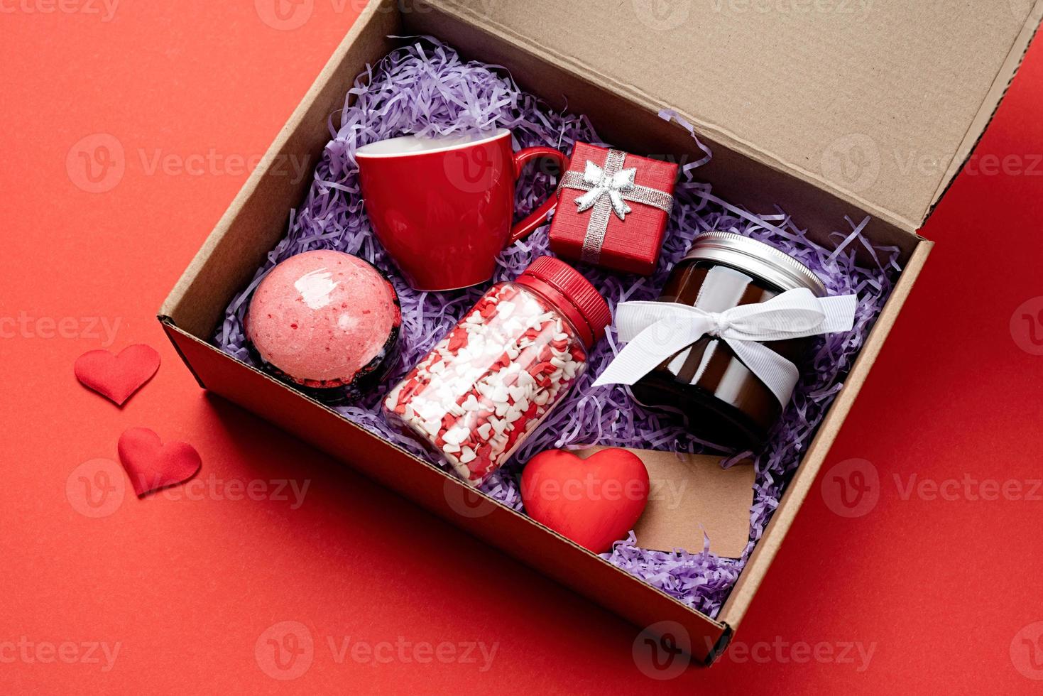 Seasonal gift box for valentine day with candle, red cup and heart shape sweets on red background photo