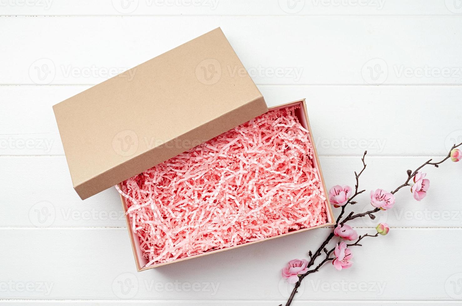 Shredded pink paper packing material texture in a craft box with sakura branch, mockup design photo