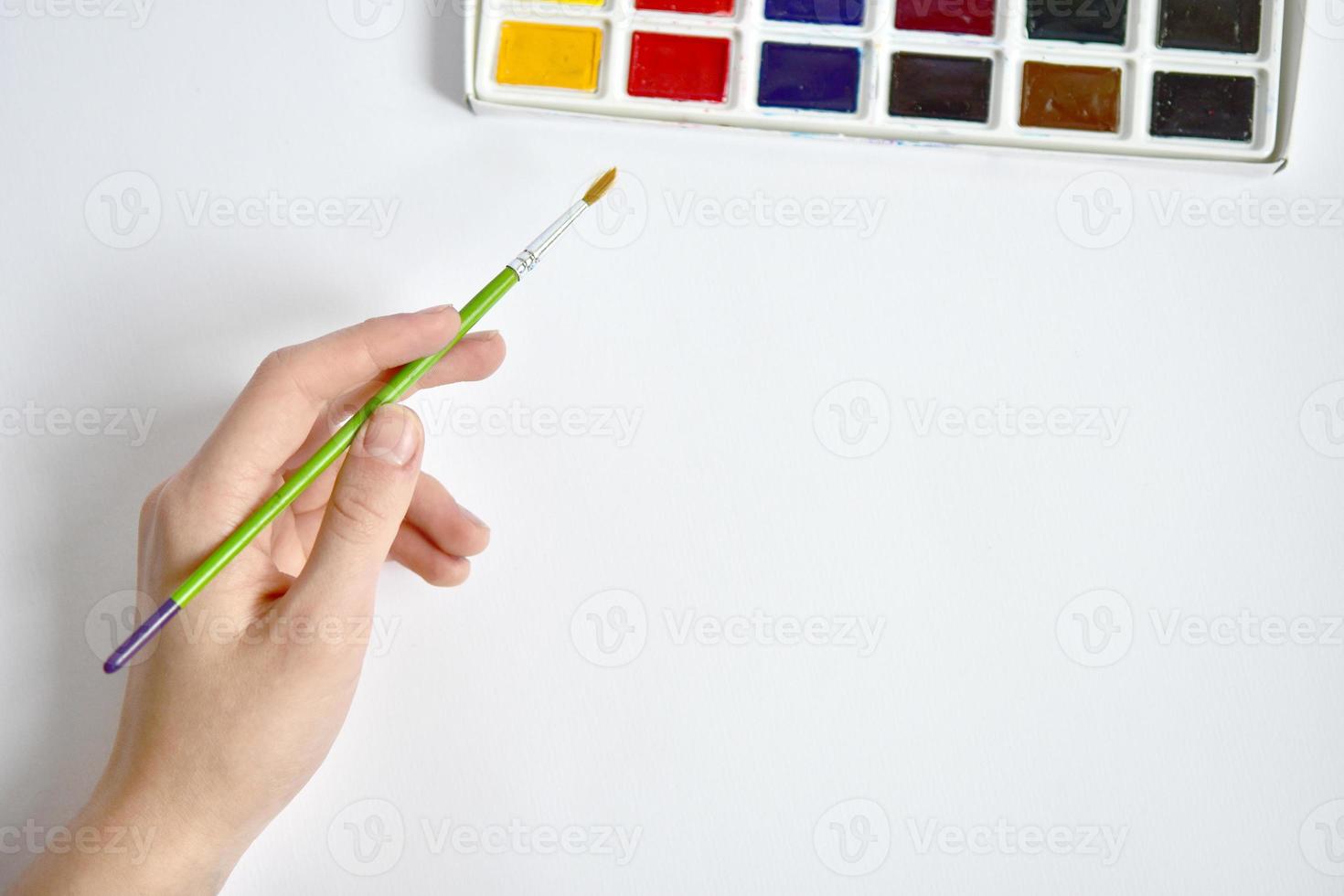 A hand with a brush reaches for watercolors. Mockup for artwork. Painting with paints photo