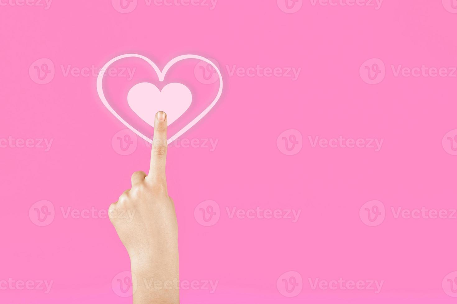 Hand on a pink background pressing on the virtual symbol of the heart. Valentine's Day photo