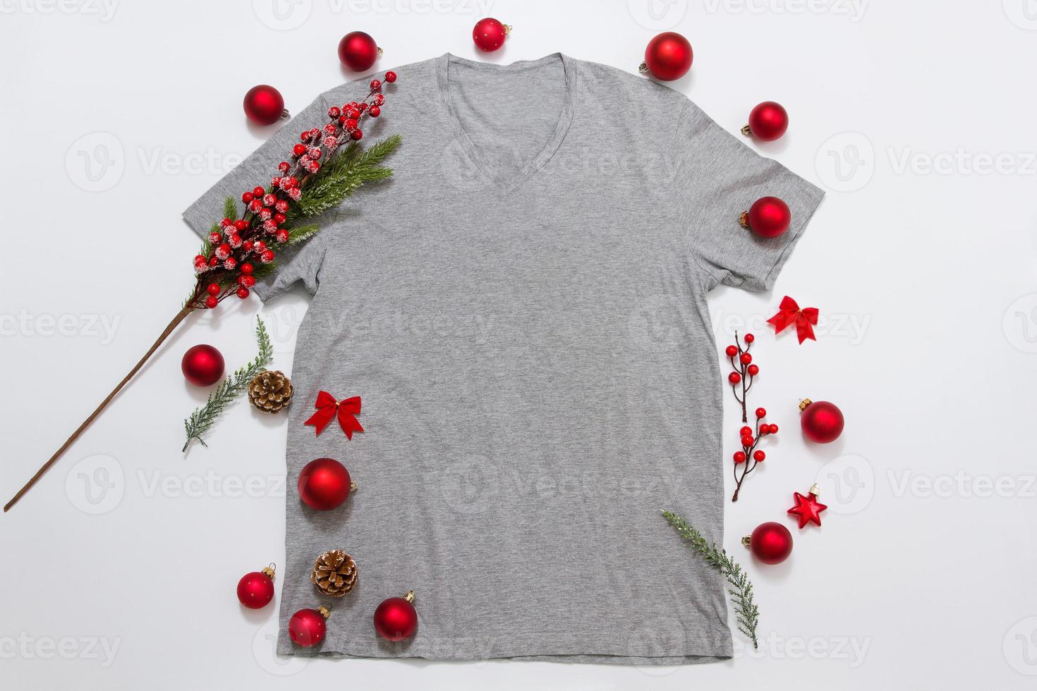 Close up grey blank template t shirt with copy space and Christmas Holiday concept. Top view mockup t-shirt and red holidays decorations on white background. Happy New Year accessories. Xmas outfit photo