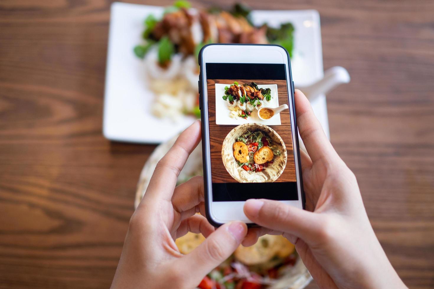 mujer que usa el teléfono móvil para tomar fotos de la comida en la mesa. tomado en el móvil y puesto en las redes sociales.